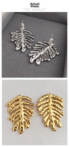 Detailed view of leaf-shaped stud earrings in polished gold and silver metal finishes
