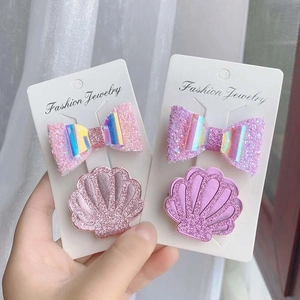 Close-up of glitter pink bow and shell hair clips for girls on white card packaging