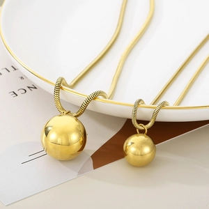 Macro shot of gold snake chains featuring polished spherical ball pendants on white ceramic
