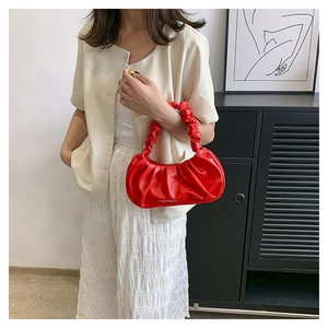 Lifestyle shot of a stylish red ruched cloud bag with handle details and white outfit