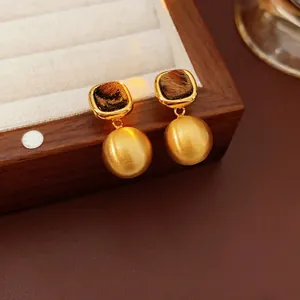 Retro gold earrings with leopard print accents and brushed metal spheres on velvet