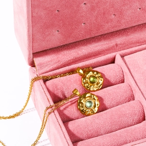 Irregular gold birthstone pendant necklace with green gem in a pink velvet box