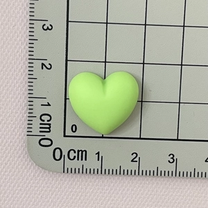 Macro view of a 1.5cm matte neon green resin heart DIY craft accessory on a grid mat