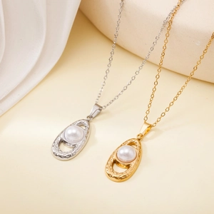 Detail of gold and silver stainless steel necklaces with oval pearl pendants on fabric
