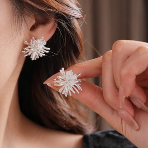 Macro shot of silver zircon earrings with fireworks design being worn on a hand