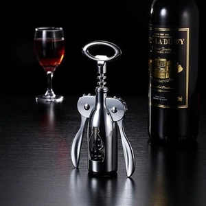 Close-up of a silver winged corkscrew opener on a dark table with red wine