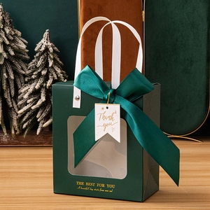Detail of dark green gift bag with transparent window, ribbon bow, and gold lettering