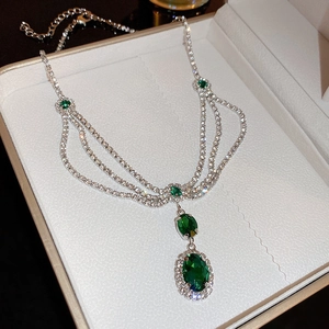 Detailed view of emerald gemstone multilayer necklace inside a beige jewelry box