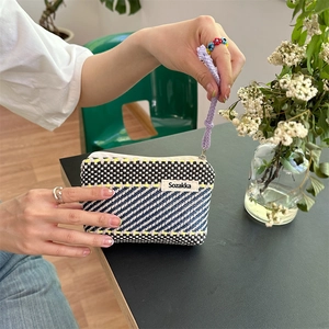 Close-up of woven geometric stripe cosmetic bag with hand strap in casual setting