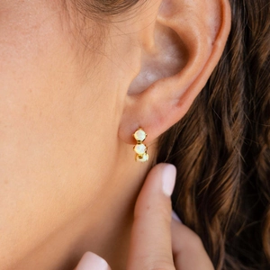 Primo piano di orecchini in oro 18k con tre pietre di opale bianco indossati sull'orecchio
