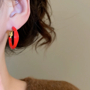 Macro detail of a model wearing red enamel hoop earrings with gold-toned metal clasps