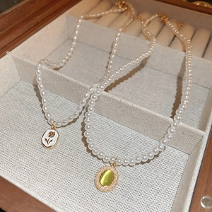 Close-up of vintage tulip enamel and green cat-eye gemstone pearl necklaces in jewelry box