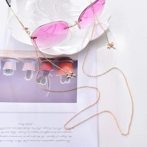 Pink rimless sunglasses with gold chain and crystal dragonfly pendant on a white tray