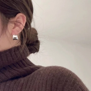 Macro side view of a model wearing minimalist silver curved stud earrings on the ear