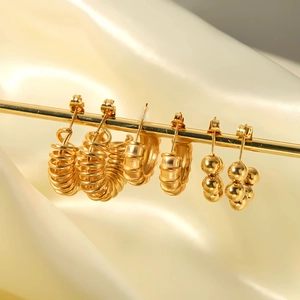 Three pairs of elegant gold titanium steel earrings displayed on beige silk fabric