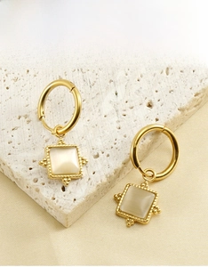 Detail of square cat eye stone earrings with gold beaded texture on a stone surface