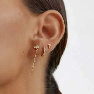 Close-up of gold stud earrings with tassel chain and zircon accents on a female model's ear