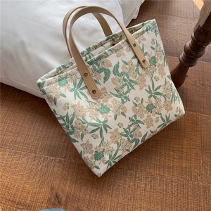 Detail of floral canvas tote bag featuring brown leather handles and vintage metal rivets