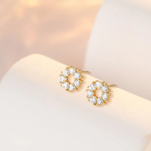 Detail of gold floral stud earrings featuring heart-shaped zircons on stone background