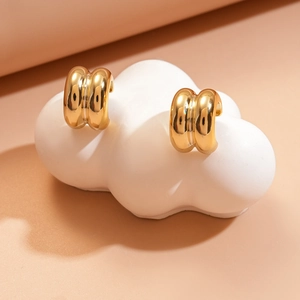 Macro shot of gold double-ribbed C-shape earrings on white cloud display stand
