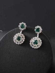 Detailed macro view of emerald and diamond earrings on a professional black display stand