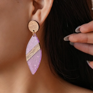 Macro shot of bohemian geometric wooden disc earrings with purple resin leaf pendants