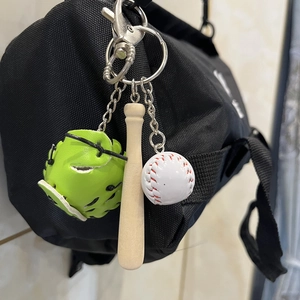 Three-piece baseball keychain with green glove, wooden bat, and white ball on a black bag