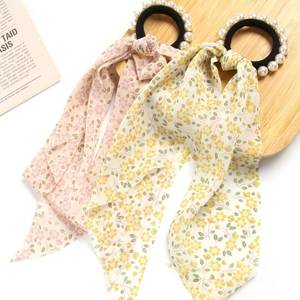Floral print hair scrunchies with long ribbons and pearl accents on a wooden tray