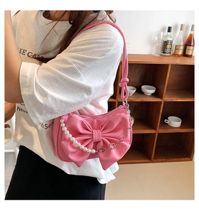 Detail view of pink shoulder bag with large bow, pearl chain and metal strap for women