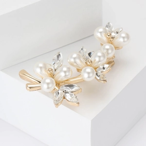Elegant gold flower brooch with white pearls and sparkling crystals on a clean white pedestal