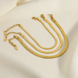 Detailed close-up of three layered flat gold snake chains on soft white silk fabric