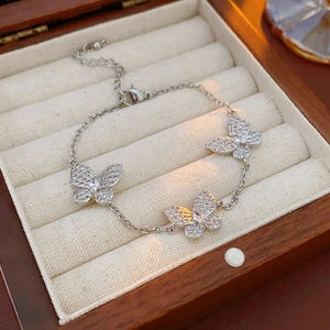 Silver butterfly bracelet with zircon pendants on beige velvet within a wooden box