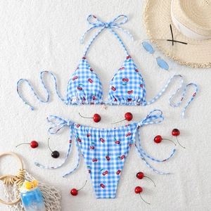 Flat lay of cherry print gingham bikini with beach hat and sunglasses on fabric
