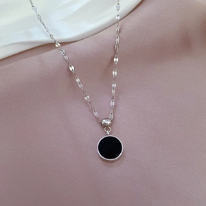 Detailed view of silver titanium steel necklace with circular black pendant on soft fabric