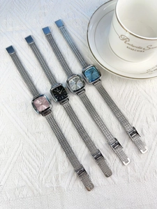 Top view of four elegant square dial watches with silver mesh straps on white fabric