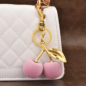 Pink flocked cherry keychain charm accessory hanging on a white quilted handbag