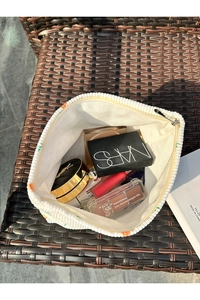 Top view of a white corduroy makeup bag filled with cosmetics on a woven chair