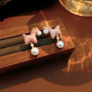 Macro detail of pink horse earrings with pearls and gold accents on a wooden stand