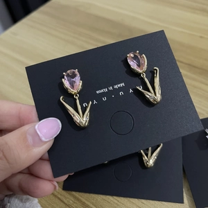 Macro view of gold tulip earrings with pink crystal petals on a black display card