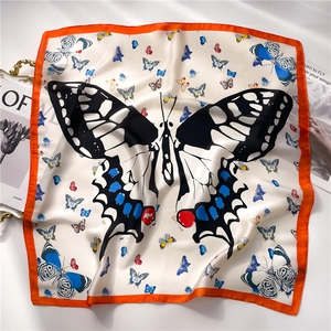 Détail macro du foulard carré effet soie avec motifs de papillons et bordures orange vif