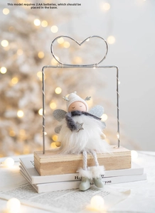 Detail of angel plush doll on wooden base with warm LED string lights and glittery wings
