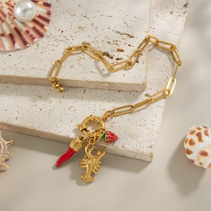 Gold paperclip chain bracelet with strawberry and lobster enamel charms on stone