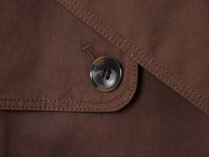 Detail of tortoiseshell button and double-stitched seams on brown trench coat fabric