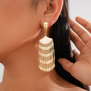 Detail shot of long golden fan-shaped tassel earrings on a model with metallic finish