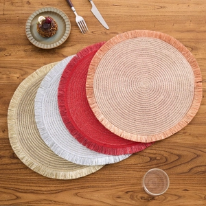 Detail of round woven placemats with tassels in gold and red on a wooden table
