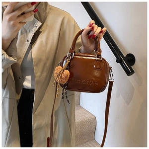 Detail of vintage brown patent leather handbag with plush bear charm and long strap