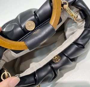Close-up of black pleated cloud bag with magnetic closure and herringbone lining
