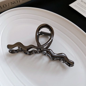 Close-up of a gun-metal grey wave-shaped hair claw clip on a white ceramic plate