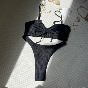 Detail eines schwarzen Bikini-Sets mit Strukturstoff, Schleifen und Strandelementen