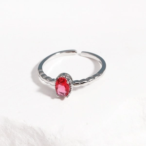 Top-down view of adjustable silver ring with an oval red zircon on white stone surface